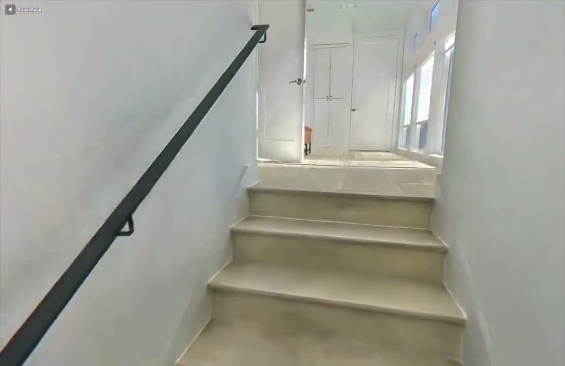 A Gaussian splat rendering of a flight of stairs with a black handrail and a hallway at the top, photorealistic but with characteristic soft edges